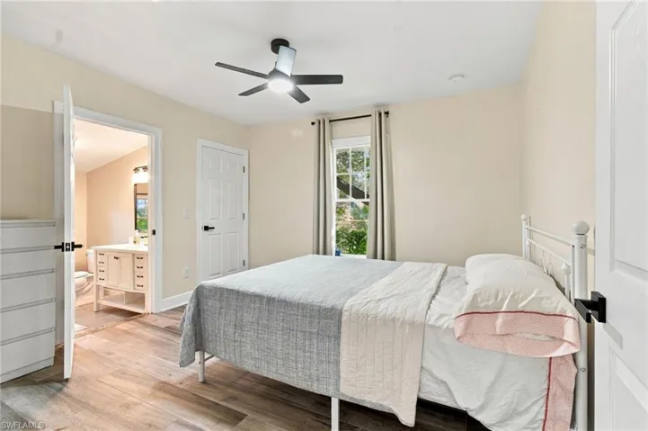 Master bedroom with private bath, featuring wood-plank tile flooring, ceiling fan with integrated lighting, and windows with drapes.