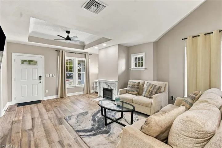 Living area featuring wood-finish flooring, a tray ceiling with a ceiling fan, a fireplace with a marble-look surround, and vaulted ceilings