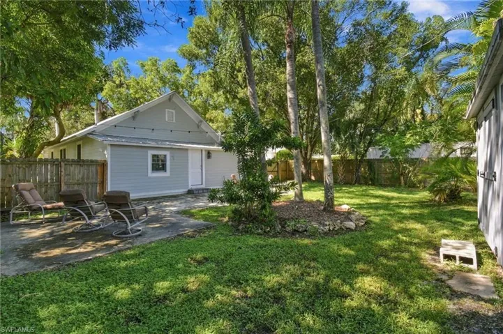 Expansive fenced in backyard with mature tress, a manicured lawn, established trees, a paver patio, with patio furniture.