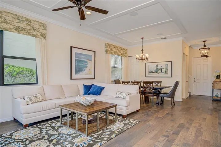 Living area featuring crown molding, dark wood-type flooring, a ceiling fan, and a chandelier