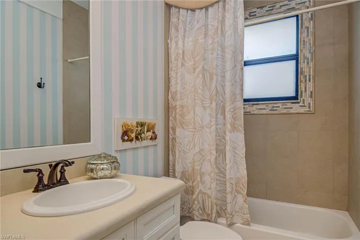 Bathroom with wallpapered walls, vanity, and shower / bathtub combination with curtain