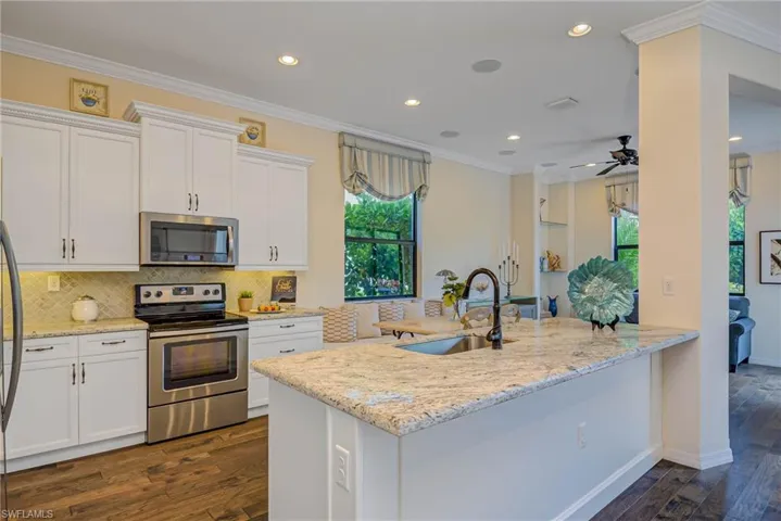 Kitchen with crown molding, stainless steel appliances, light stone counters, white cabinetry, and dark wood-style floors