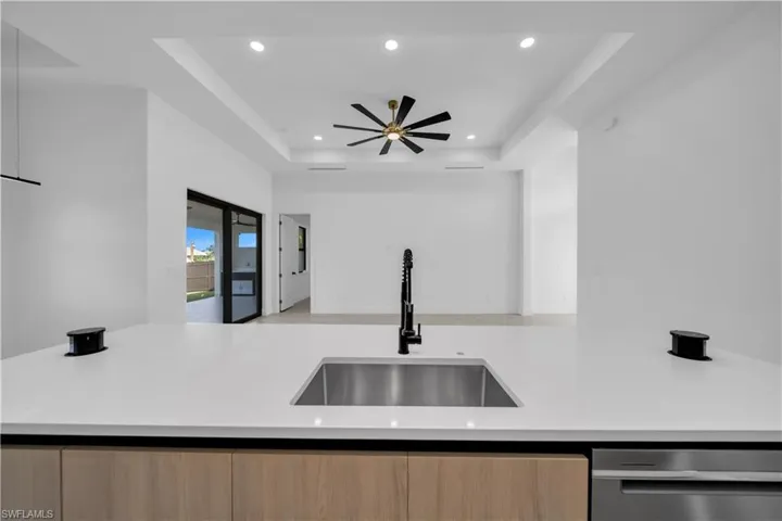 Kitchen island featuring a white countertop, undermount stainless steel sink, and matte black pull-down faucet, highlighted by a recessed tray ceiling with integrated lighting and a multi-blade ceiling fan