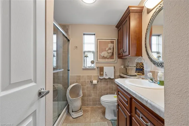 Bathroom featuring tile patterned floors, walk in shower, vanity, tile walls, and toilet