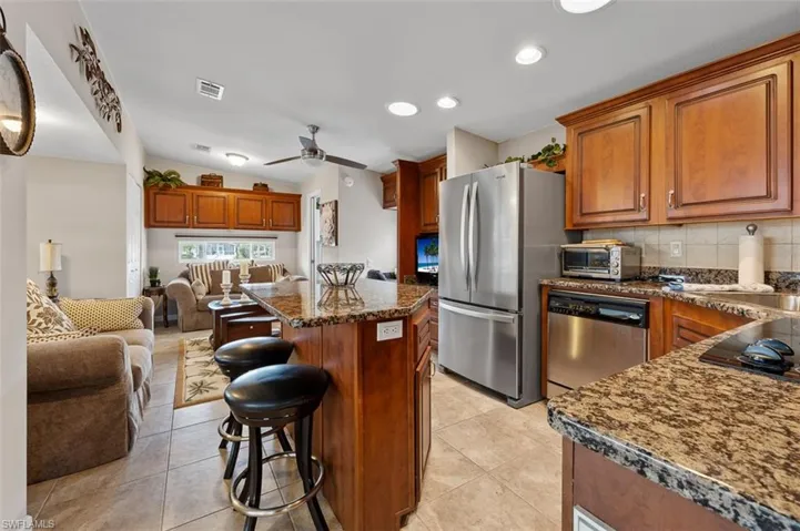 Kitchen with decorative backsplash, stainless steel appliances, ceiling fan, a kitchen island, and a breakfast bar area