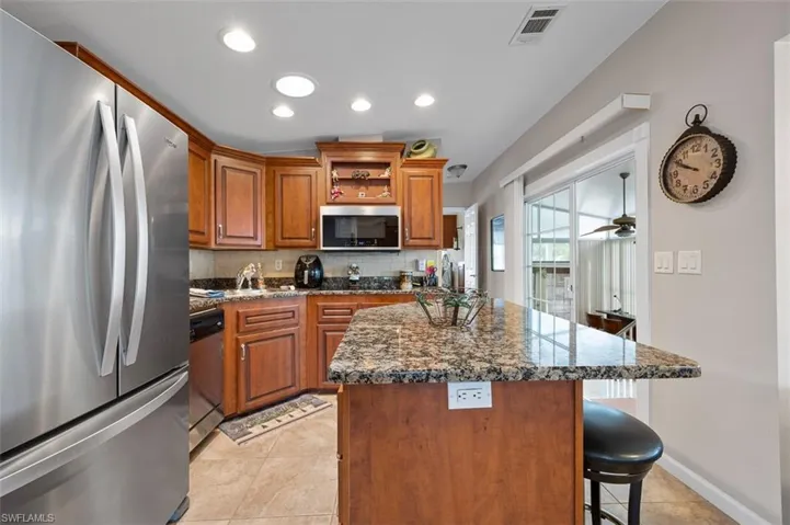 Kitchen featuring stainless steel appliances, tasteful backsplash, dark stone counters, a breakfast bar, and a kitchen island