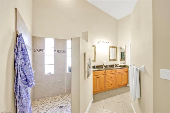 Bathroom with tile patterned floors, double vanity, baseboards, high vaulted ceiling, and a walk in shower