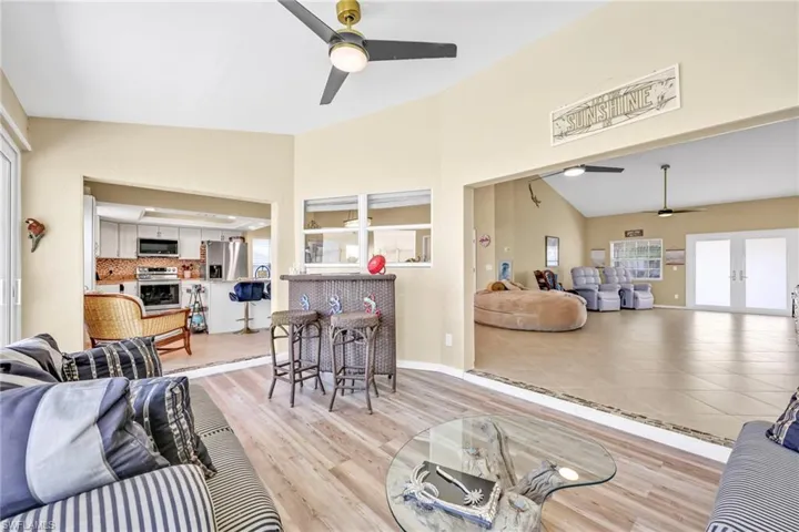 Living area with high vaulted ceiling, light wood-style floors, ceiling fan, french doors, and baseboards