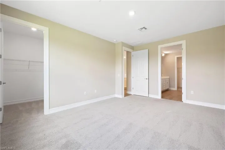 Unfurnished bedroom featuring carpet flooring, a closet, ensuite bath, and a walk in closet