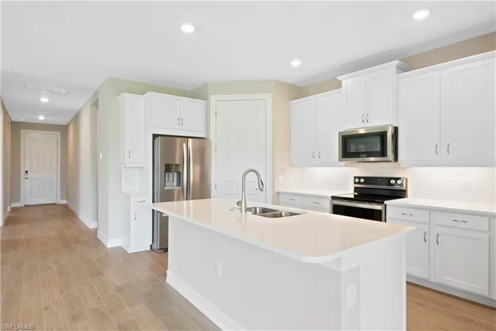 Kitchen featuring stainless steel appliances, a center island with sink, sink, backsplash, and white cabinetry
