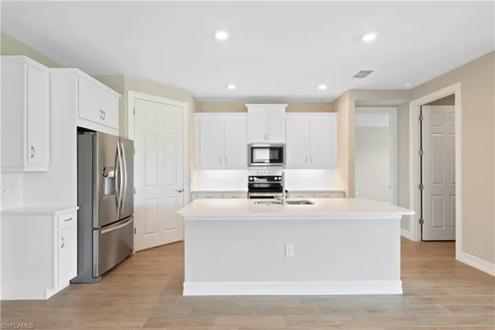 Kitchen with white cabinetry, stainless steel appliances, light wood-type flooring, an island with sink, and sink