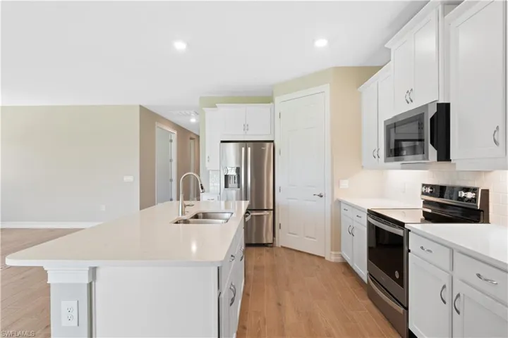Kitchen featuring light hardwood / wood-style flooring, a kitchen island with sink, stainless steel appliances, decorative backsplash, and sink