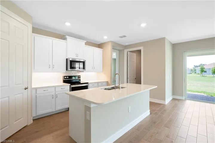 Kitchen featuring white cabinetry, backsplash, appliances with stainless steel finishes, and an island with sink