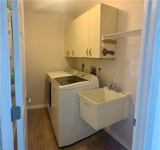 Clothes washing area featuring washing machine and clothes dryer, cabinets, sink, and dark wood-type flooring