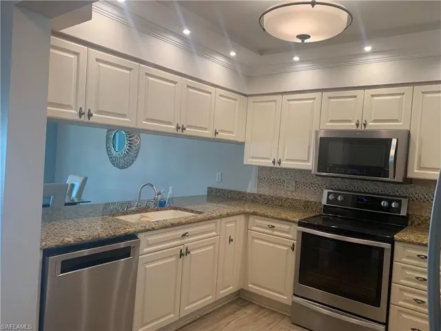 Kitchen featuring backsplash, sink, light stone countertops, white cabinetry, and stainless steel appliances