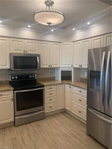 Kitchen with white cabinets, light stone counters, stainless steel appliances, and tasteful backsplash
