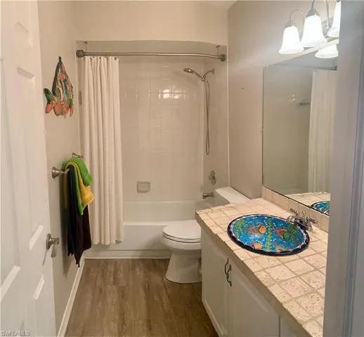 Full downstairs bathroom with shower / tub combo, vanity, hardwood / wood-style flooring, and toilet