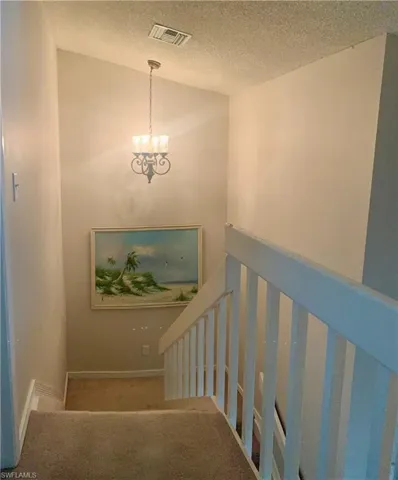 Stairs featuring carpet flooring, a textured ceiling, and a notable chandelier