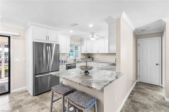 Kitchen featuring stainless steel appliances, light stone counters, white cabinetry, ornamental molding, and a peninsula