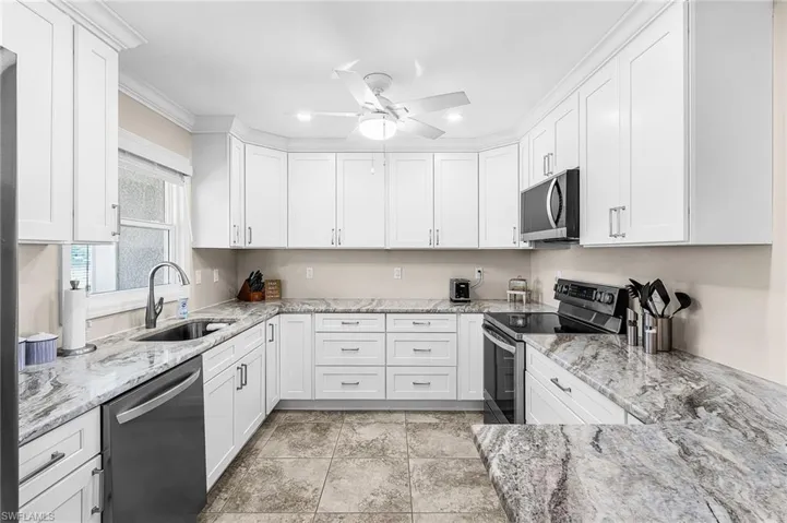 Kitchen with stainless steel appliances, light stone countertops, white cabinets, a ceiling fan, and crown molding