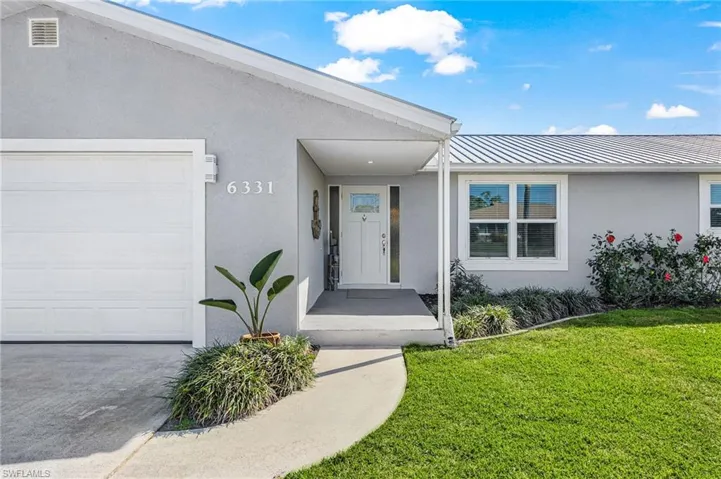 View of exterior entry with stucco siding, a metal roof, a yard, and an attached garage