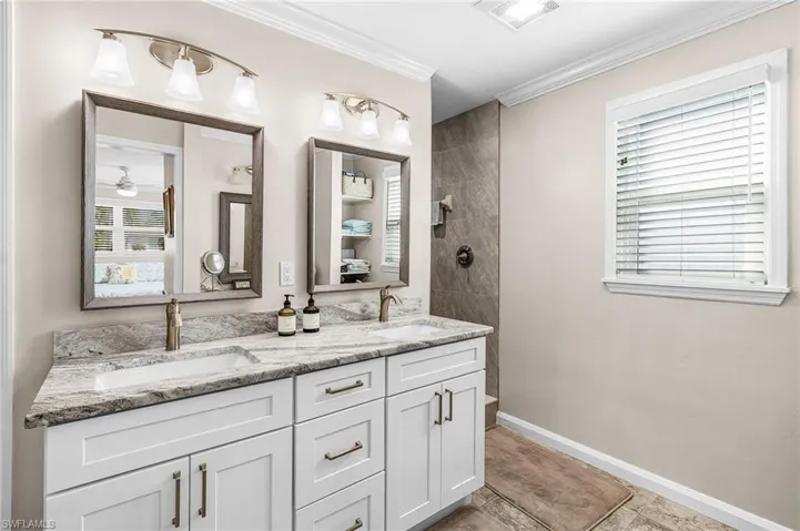 Full bathroom featuring double vanity, ornamental molding, light tile patterned floors, and a tile shower