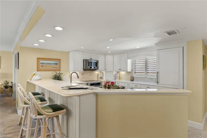 Kitchen with tasteful backsplash, crown molding, stainless steel appliances, a peninsula, and white cabinets