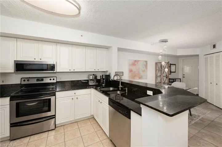 Kitchen with appliances with stainless steel finishes, a textured ceiling, dark stone counters, a peninsula, and white cabinets