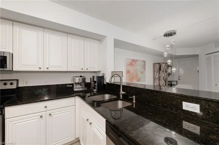 Kitchen featuring dark stone countertops, appliances with stainless steel finishes, white cabinets, and a textured ceiling