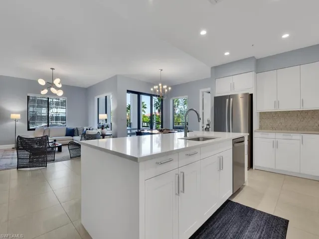 Kitchen with a chandelier, white cabinetry, stainless steel appliances, a center island with sink, and light stone countertops