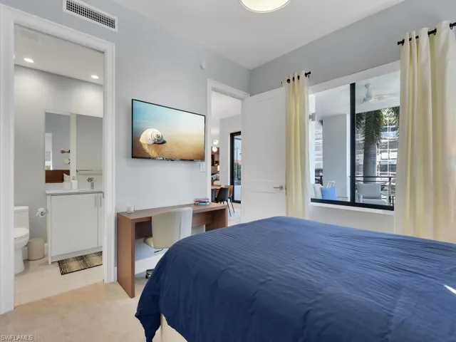 Bedroom with an office area, connected bathroom, and light carpet