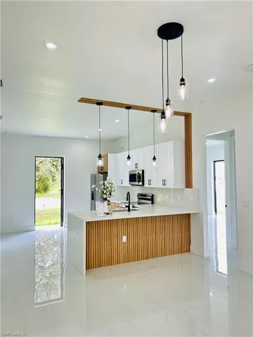 Gourmet kitchen with white cabinetry, black hardware, stainless steel appliances, and a quartz countertop island with wood-finish paneling