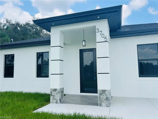 White stucco exterior with black-framed windows, a black entry door, and stone accents on the front column