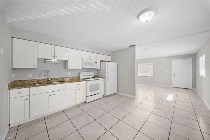 Kitchen with white appliances, white cabinets, healthy amount of natural light, and a textured ceiling