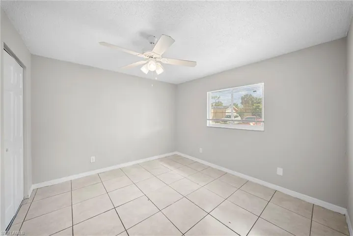 Unfurnished bedroom featuring a closet, a textured ceiling, ceiling fan, and light tile patterned floors
