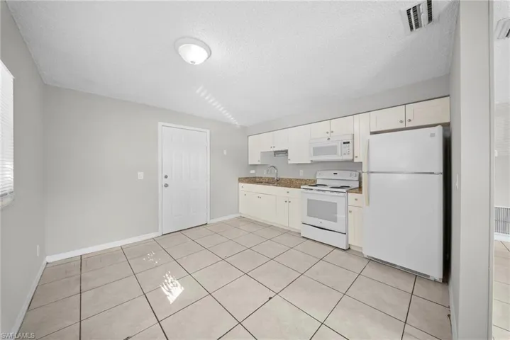 Kitchen featuring white appliances, a textured ceiling, white cabinetry, and light tile patterned floors