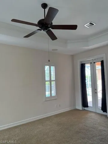 Carpeted empty room with crown molding, french doors, ceiling fan, baseboards, and a raised ceiling