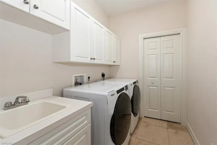 Laundry area with cabinet space, washer and dryer, light tile patterned flooring, and baseboards