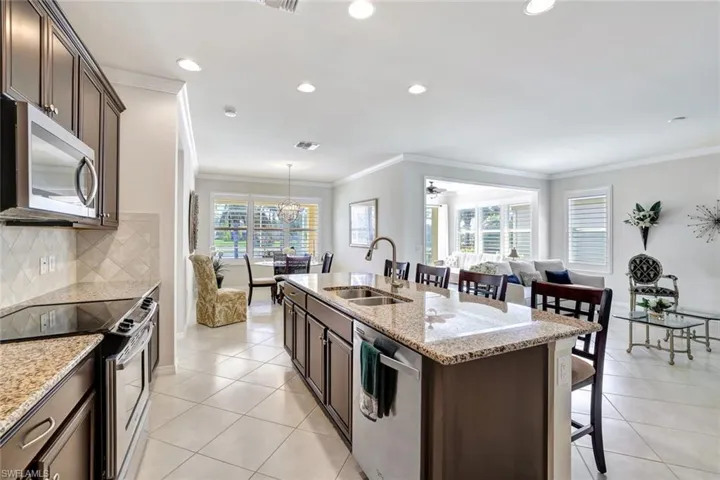 Kitchen with a center island with sink, appliances with stainless steel finishes, light tile patterned flooring, a sink, and light stone countertops