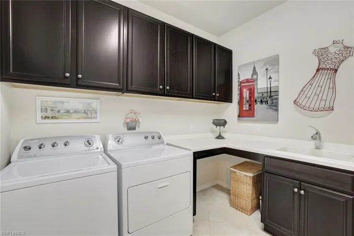Laundry area featuring light tile patterned floors, washing machine and clothes dryer, a sink, and cabinet space