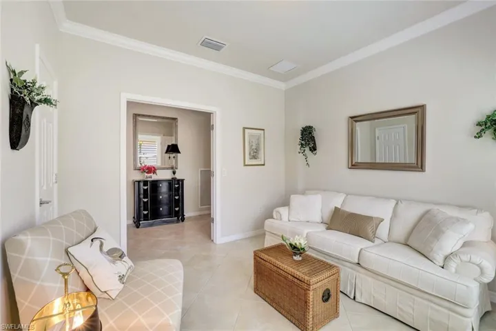 Living area with light tile patterned floors, baseboards, visible vents, and crown molding