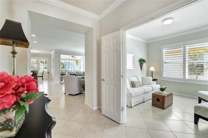 Living room featuring light tile patterned floors, ceiling fan, ornamental molding, and baseboards