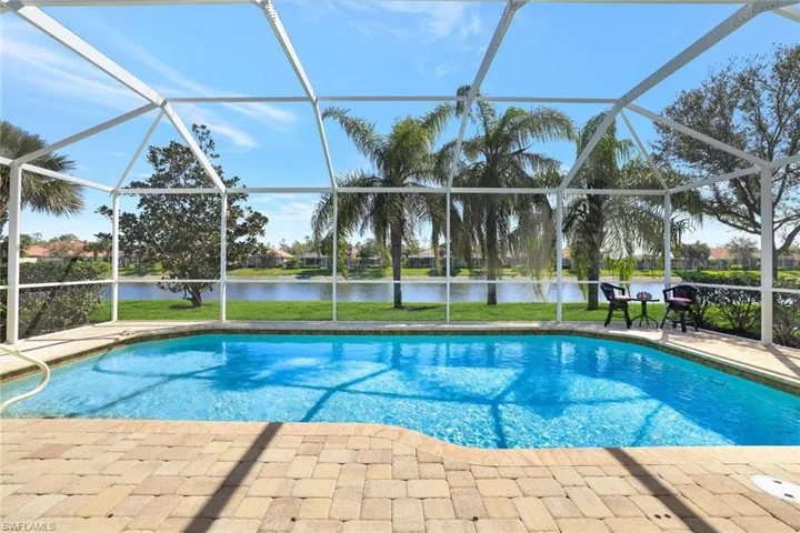 Pool with a water view, glass enclosure, a patio area, and a lawn