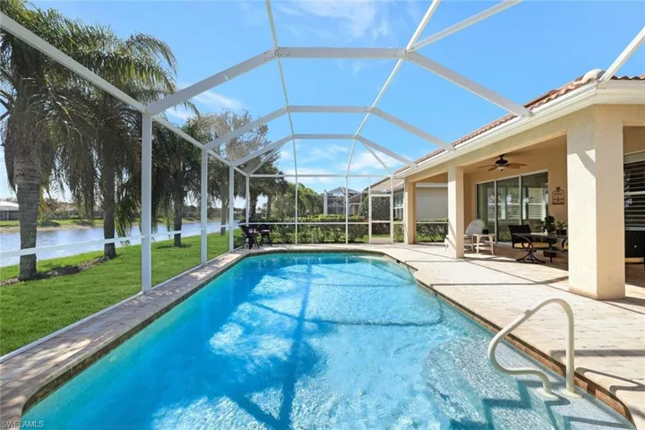 Outdoor pool featuring a lanai, a water view, a ceiling fan, a yard, and a patio area