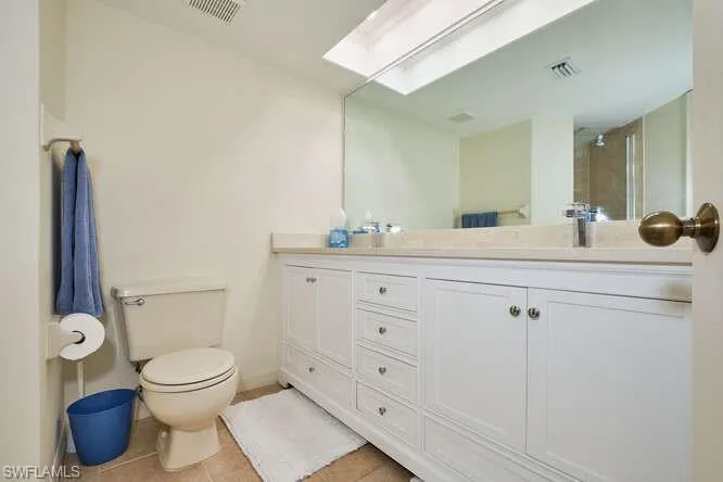 Bathroom with toilet, a skylight, tile patterned flooring, and visible vents
