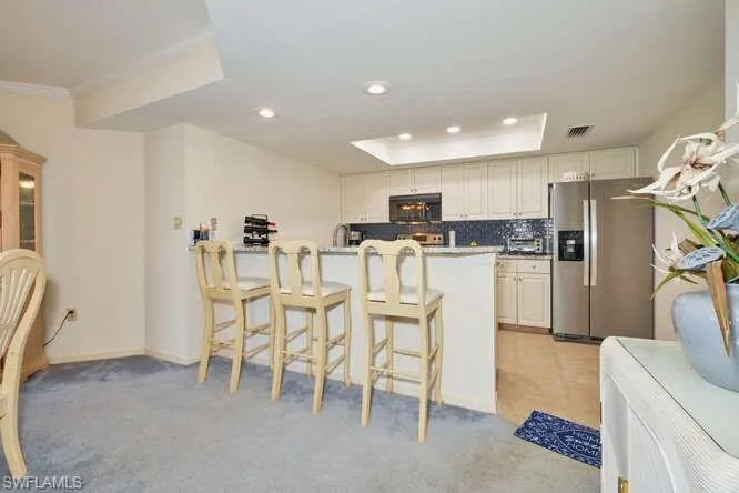 Kitchen featuring black microwave, a kitchen breakfast bar, stainless steel refrigerator with ice dispenser, decorative backsplash, and a raised ceiling