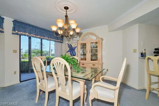Carpeted dining space with baseboards, ornamental molding, and an inviting chandelier
