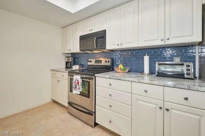 Kitchen featuring a toaster, tasteful backsplash, white cabinets, electric stove, and black microwave