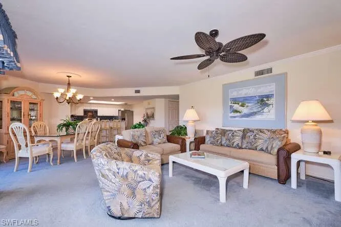 Living room featuring carpet floors, visible vents, crown molding, and ceiling fan with notable chandelier