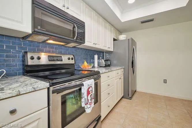 Kitchen with a tray ceiling, visible vents, backsplash, appliances with stainless steel finishes, and light tile patterned flooring